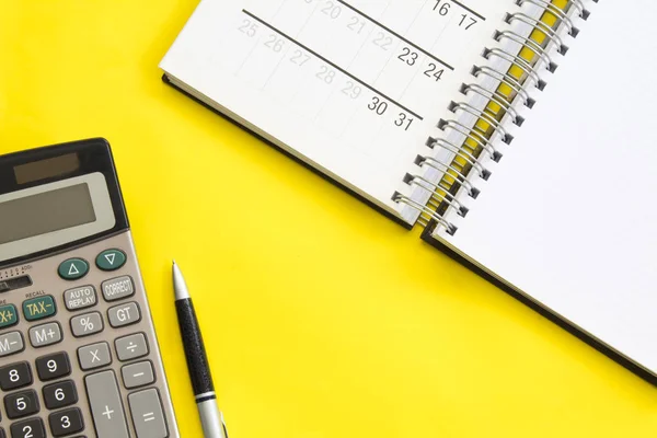 Muhasebe, finansal kavramı, kalem düz yatıyordu veya üst görünümünü, canlı sarı arka plana tablo boş kopya alanı, takvim, matematik, maliyet, vergi veya yatırım hesaplama ile beyaz Not defteri ile hesap makinesi.