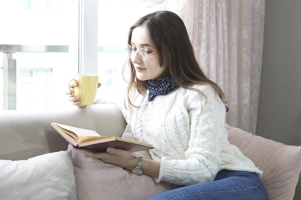 Oturma odasında elinde kahveyle kitap okuyan bir kadın.