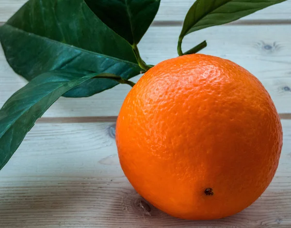 Single orange fruit with leaves on the wooden table