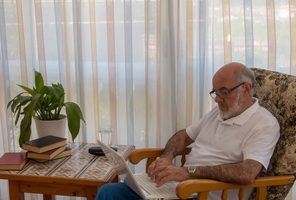 Yaşlı adam dizüstü bilgisayar ile sandalyede oturan