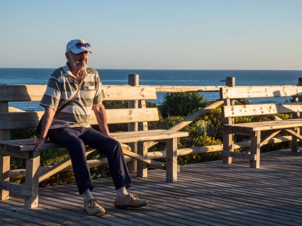 Denize yakın bankta yaşlı adam, gün batımı