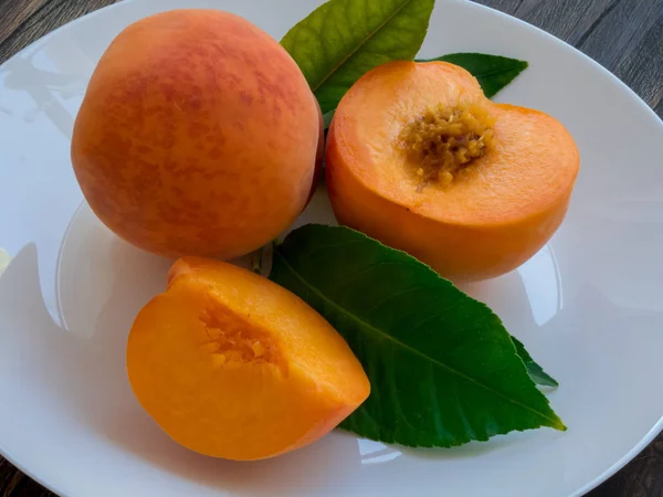 Yellow peaches full and cut on white plate with green leaves, on