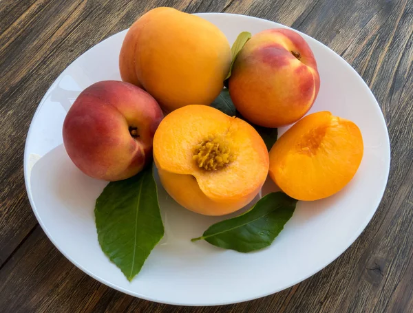 Yellow peaches full and cut on white plate with green leaves, on — Stock Photo, Image
