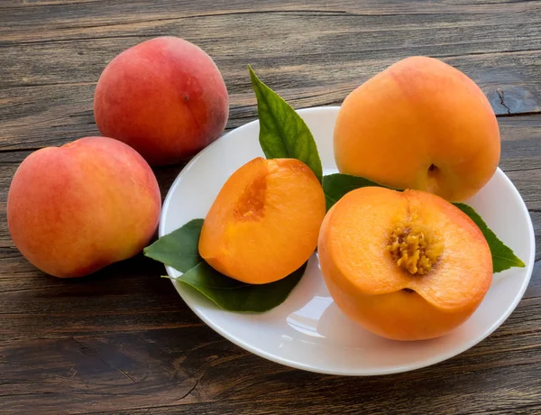 Yellow peaches full and cut on white plate with green leaves, on