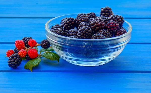 Blackberry fruit  in glass bowl on wooden blue table, berries on