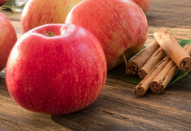 Yeşil yaprakları üzerinde tarçın çubukları ile kırmızı ve pembe elma 