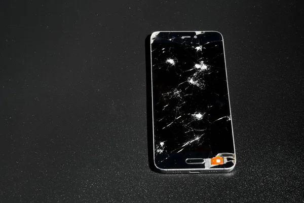 Cell phone with broken screen on dark background.