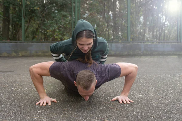 A fit man push-ups during training with a girl on his back