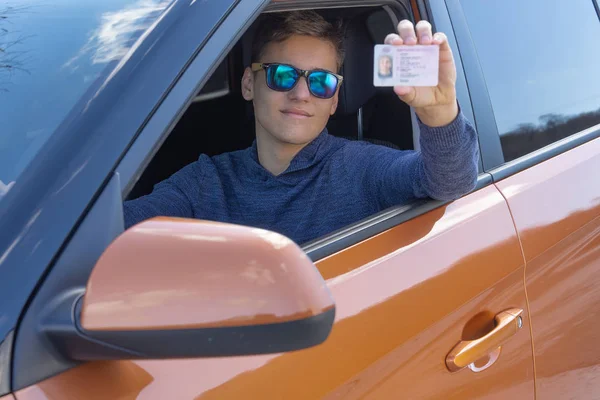 Feliz adolescente está mostrando su licencia de conducir desde la ventana abierta del coche. Concepto de escuela de conducción — Foto de Stock