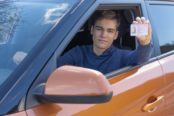 A teenager is sitting in new car and shows his drivers license. Concept Driving school