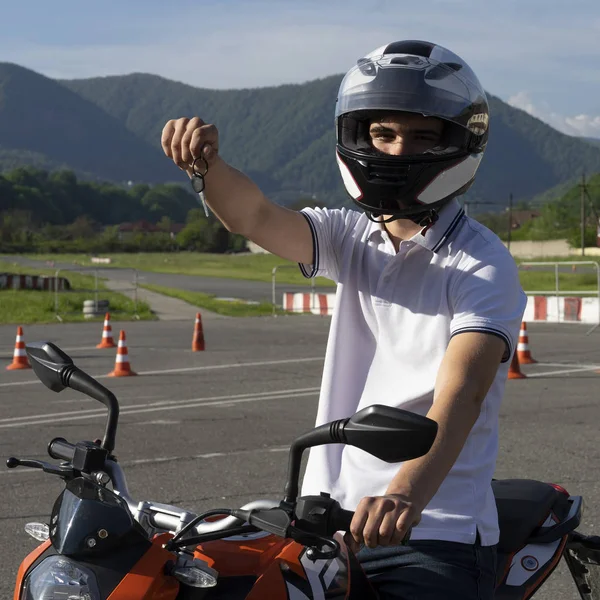 Man in a helmet on a motorbike shows key from motorcycle. Concept driving school