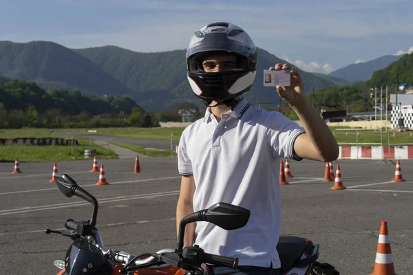 Motosikletli kasklı genç adam ehliyetini gösteriyor.