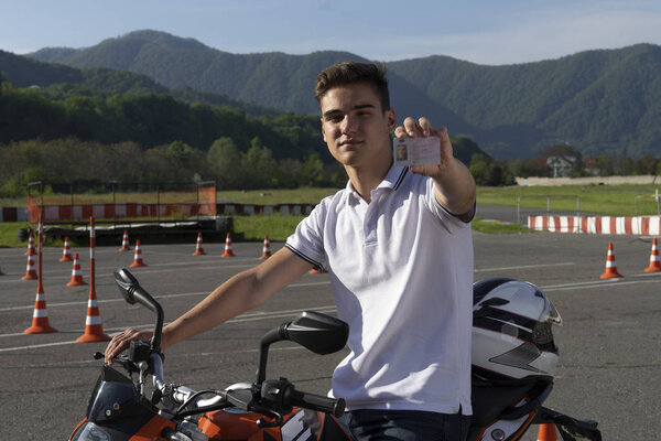 A young man graduated from the driving school, he shows driving licence for motorcycle