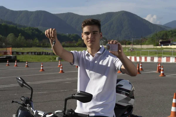 Young man on the motorbike is showing driving license and motorcycle keys. Motorcycle school