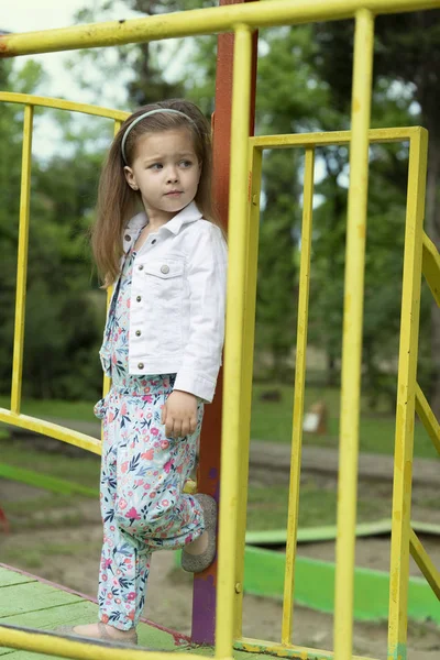 La mode du gamin. Petite fille dans les choses à la mode pose sur l'aire de jeux. Belle petite fille de trois ou quatre ans se fait passer pour un mannequin . — Photo