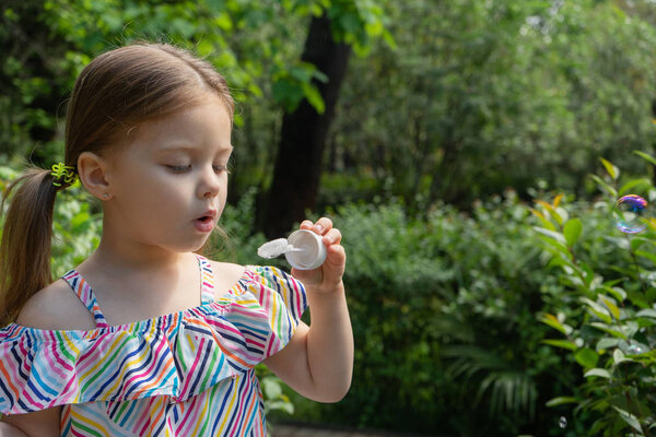 Милая маленькая девочка надувает мыльные пузыри в саду
