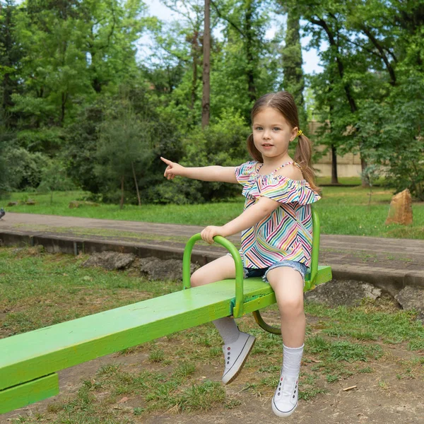 Petite fille blonde de trois à quatre ans sont des promenades sur les balançoires sur le terrain de jeux — Photo