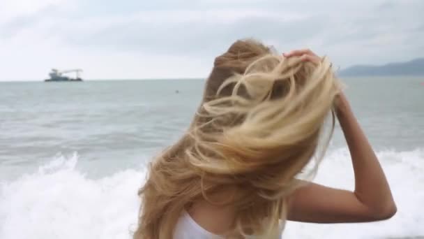 ブロンドの女性の背中からの眺め スローモーションで空気中の髪の柔らかい動き ブロンドの女の子が浜辺を歩いている クローズ アップ — ストック動画