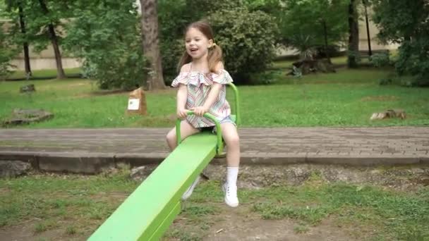 Hermosa Niña Rubia Teeter Chico Está Montando Columpios Parque Infantil — Vídeos de Stock