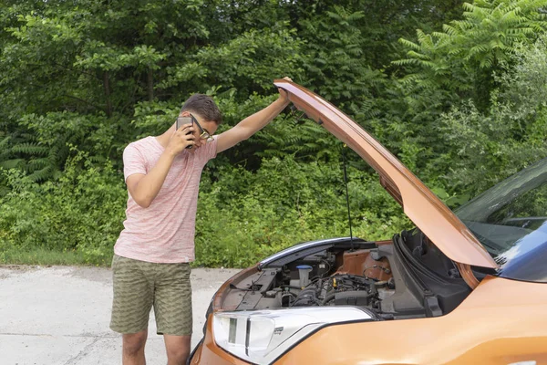 Vehicle trouble. A young man opens the hood, looking inside, rummaging in the engine. Man calls and asks for help on the road