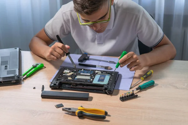 Um jovem especialista repara um laptop com uma chave de fenda e um ferro de solda — Fotografia de Stock