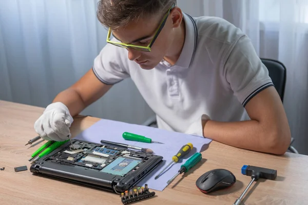 Jovem engenheiro masculino repara um laptop. Conceito de serviço de reparação eletrônica . — Fotografia de Stock
