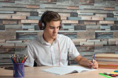 Left-handed-students sitting at desk in headphone and doing his homework clipart