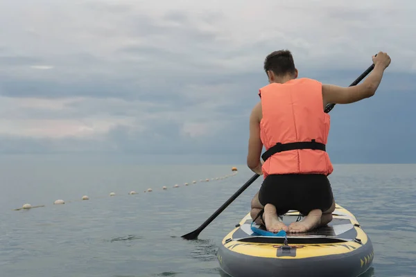 Beginner surfer in the life jacket is preparing to learn to sup surf on calm water. Safety of water recreation