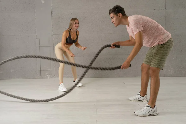 Fitness coach and her client doing functional training with battle rope in fitness club