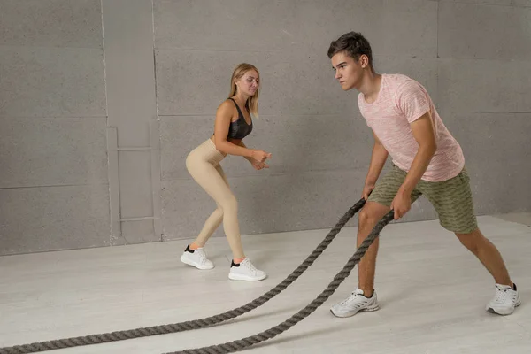 Young man and woman at functional fitness training in gym doing sport with battle ropes. Personal trainer shows how to use battle ropes for endurance training
