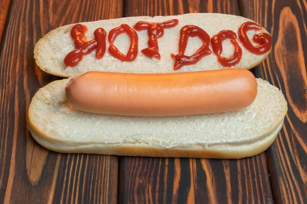 Pan de perrito caliente con salchicha sobre fondo de madera oscura. La inscripción ketchup Hot-dog. Vista superior . —  Fotos de Stock