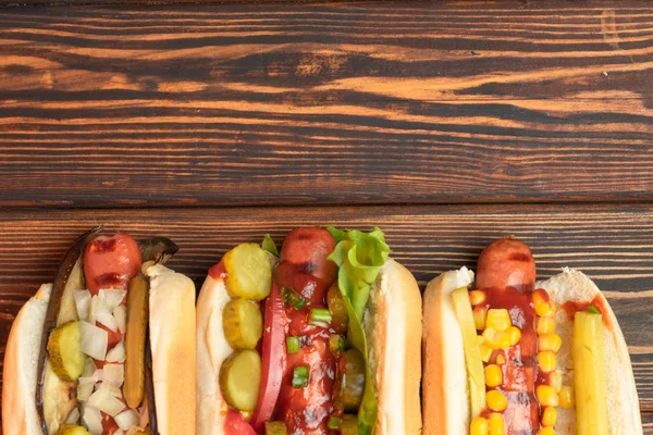 Três cachorros-quentes fritos em um fundo de madeira escura. Fast food, almoço de negócios. refeição de rua. Espaço de cópia — Fotografia de Stock