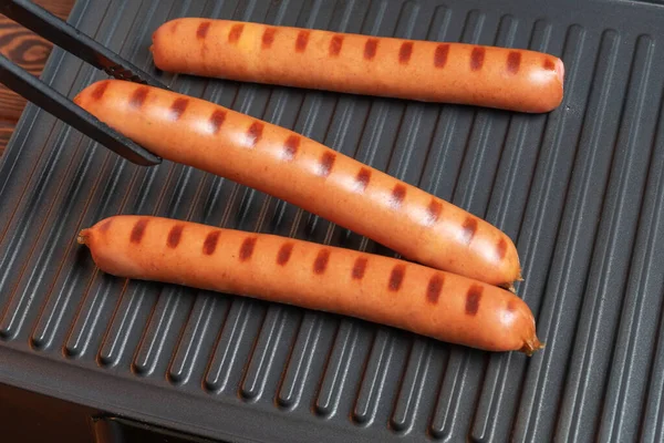 Barbecue sausages on electric grill, cooking hot dogs on BBQ with forceps. — Stock Photo, Image