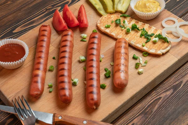 Барбекю, смажені ковбаски Hot Dog з гірчицею, кетчупом та овочами: цибулею, соліннями, помідорами на темному дерев'яному столі. барбекю — стокове фото