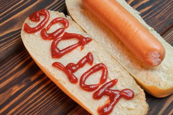 Hot dog with a fried sausage on dark wooden background. The inscription ketchup Hot-dog. Top view. Macro — Stock Photo, Image