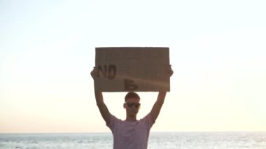 Öğrenci elinde karton bir poster tutuyor. B gezegeni yok, deniz arka planında..