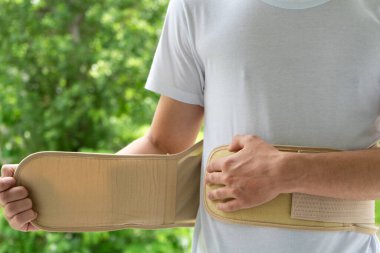 A person who wears an orthopedic lumbar corset against the background of nature, supports the back for the back muscles during active rest. Back brace.