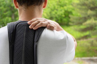 Erkek vücudunda ortopedik korse, sırt korsesi. Yeşil doğal bir arka planda omurga düzelticisi olan genç. Kas gücü desteği