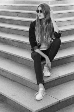 Kot takım elbiseli bir kızın merdivenlerde oturduğu siyah beyaz bir görüntü. Merdivenlerde oturan şık güzellik mankeni kız. Retro biçimi.