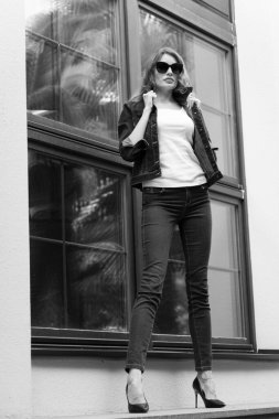 Kot takım elbiseli uzun saçlı bir mankenin siyah beyaz fotoğrafı. Topuklu giyen uzun kız.