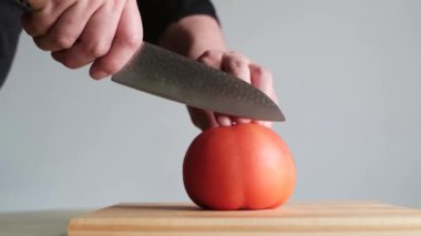Genç adam olgun kırmızı bir domatesi tahta bir tahtanın dört parçasına ayırıyor. Taze ve sağlıklı yiyecekler. Yavaş çekim.
