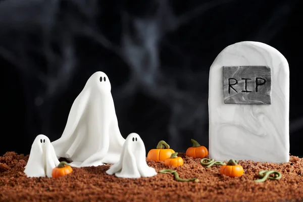 Sugar paste scene of halloween, a cute family of ghosts next to a grave, surrounded by pumpkins, chocolate cake ground, dark textured background
