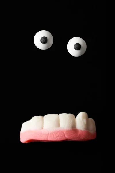 Funny creature, halloween monster, sugar eyes and gummy teeth on a black background