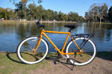 Buenos Aires, Arjantin 'deki Bosques de Palermo olarak bilinen büyük halk parkında bir gölün kenarında turuncu bisiklet.