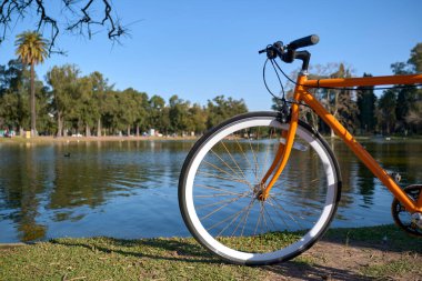 Buenos Aires, Arjantin 'deki Bosques de Palermo olarak bilinen büyük halk parkında bir gölün kenarında turuncu bisiklet.