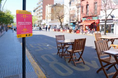CABA, Buenos Aires / Argentina; Sept 19, 2020: tables set up on the street, separated from each other, and signs encouraging social distance, to avoid contagion during the coronavirus pandemic clipart