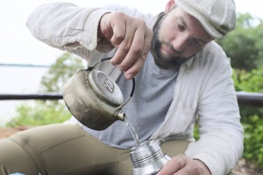 İspanyol bir adam sıcak suyu çaydanlıktan termosa boşaltıyor, açık havada..