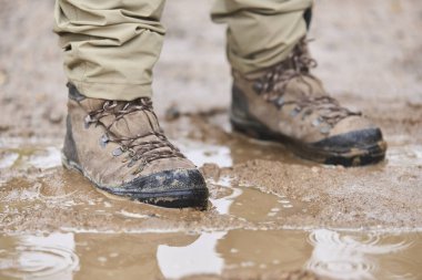 Bilinmeyen gezgin yağmurlu bir günde doğada duruyor. Çamur ve su birikintileriyle çevrili deri botlarının görüntüsü.