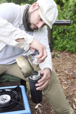 Adam, çaydanlıktan termosa sıcak su döküyor. Konsept: doğa tatili