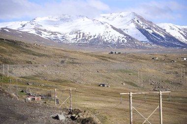 Snowcapped peaks of the imposing Andes mountains rising above the vast, arid patagonian steppe and some rural dwellings during wintertime; Neuquen, Argentina.